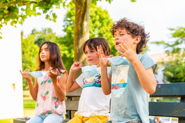 Enfants assis sur un banc enlevant leurs masques chirurgicaux à l'extérieur