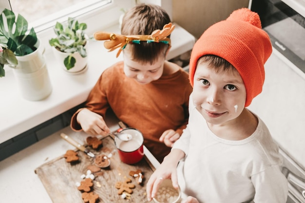 Les enfants boivent du cacao avec des guimauves et un bonhomme en pain d'épice de Noël sur un fond en bois. Vacances d'hiver à la maison. Moment de plaisir dans la cuisine. 2 garçons avec des bois cuisinent dans la cuisine