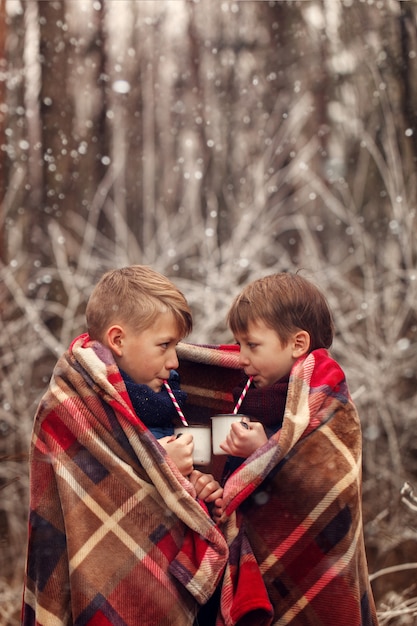 Les enfants boivent du chocolat chaud sous une couverture chaude dans la forêt de l'hiver. Vacances de Noël.