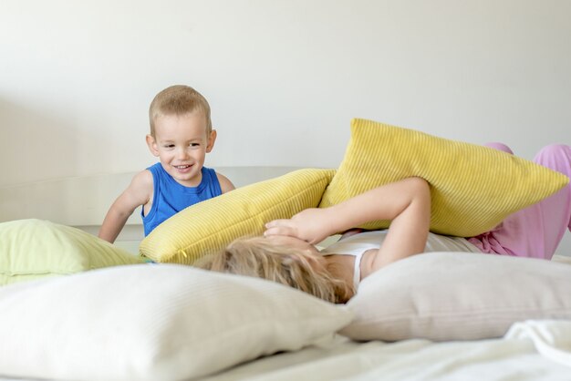 Enfants caucasiens jouant avec des oreillers sur le lit