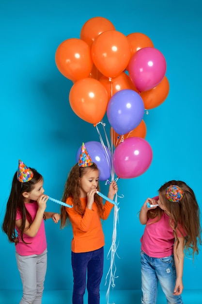 Enfants en chapeau d'anniversaire avec des ballons à air colorés et lumineux soufflant une corne de fête