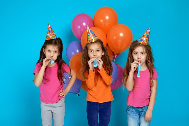 Enfants en chapeau d'anniversaire avec des ballons à air colorés et lumineux soufflant une corne de fête