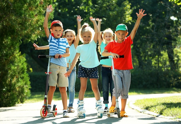 Enfants à Cheval Sur Des Scooters Et Des Patins à Roulettes Dans Le Parc