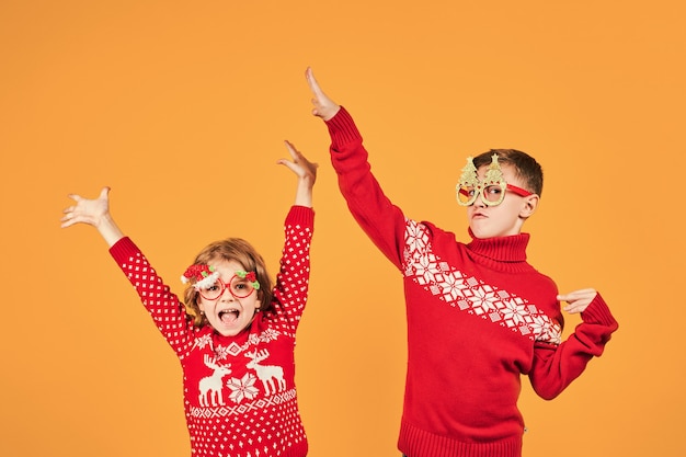 Enfants confiants dans les chandails de Noël rouge chaud et verres décorés en regardant la caméra sur fond jaune