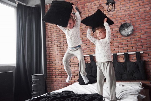 Enfants coquins Un petit garçon et une fille ont organisé une bataille d'oreillers sur le lit de la chambre. Ils aiment ce genre de jeu