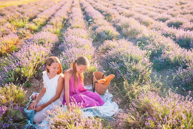 Enfants dans le champ de fleurs de lavande au coucher du soleil en robe blanche et chapeau