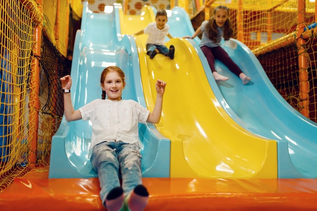 Les enfants descendent la colline dans le centre de divertissement. Loisirs filles et garçons en vacances, bonheur de l'enfance, enfants heureux sur l'aire de jeux