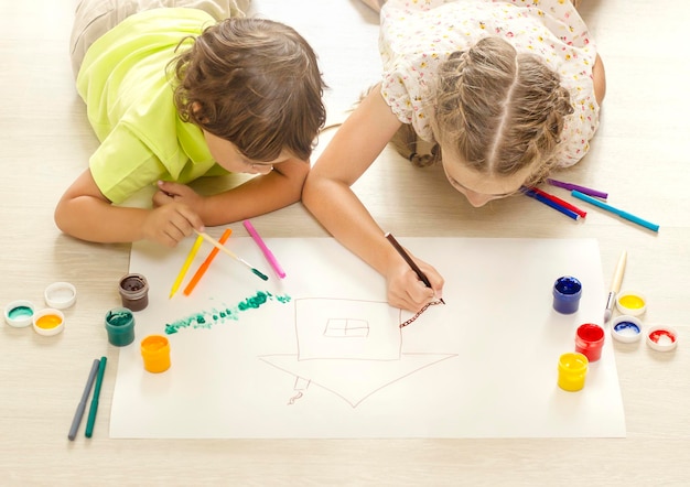 les enfants dessinent avec des peintures gisant sur le sol Vue d'en haut