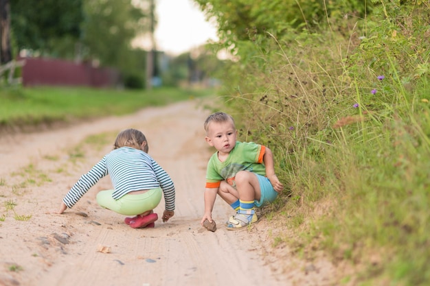 Les enfants dessinent avec une pierre sur le sable en s'accroupissant sur une route de village sablonneuse.