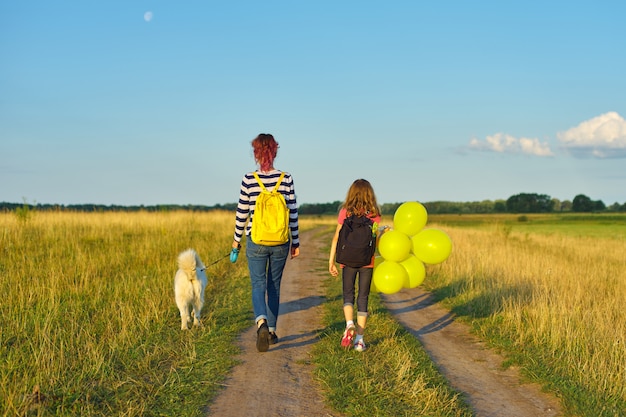 Enfants deux filles marchant le long d'une route de campagne avec chien et ballon, vue arrière