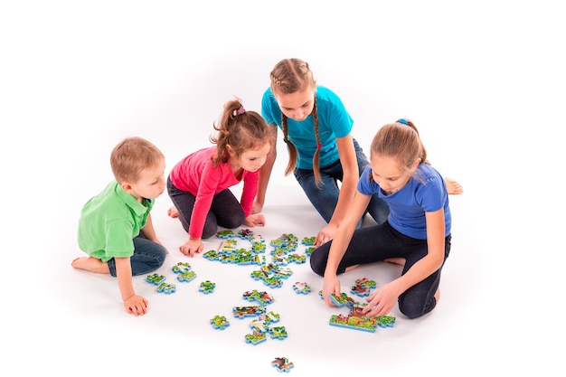 Les enfants de différents âges résolvent des puzzles ensemble. Travail d'équipe, travailler ensemble, résoudre le concept de problèmes