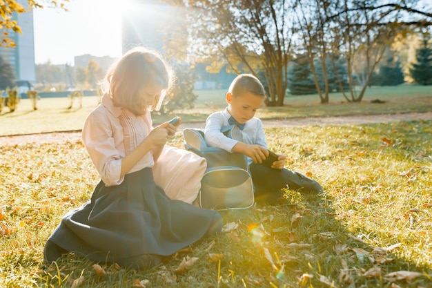 Les enfants de l'école garçon et fille s'asseoir dans le parc en automne sur l'herbe