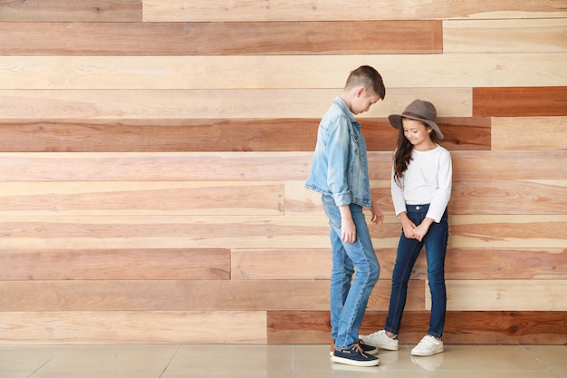 Enfants élégants en jeans près du mur en bois