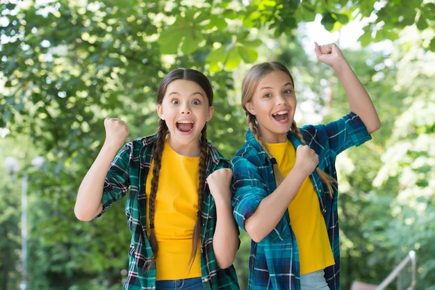 Des enfants énergiques et heureux font des gestes gagnants dans un paysage d'été de style décontracté à l'extérieur gagnants