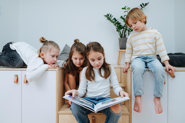 Des enfants ennuyés se sont réunis dans une pièce pour lire un livre d'images tout en le regardant De cinq à huit ans