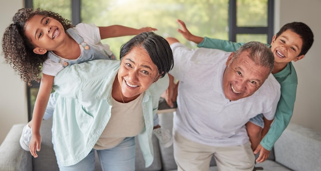 Les enfants de la famille et le dos avec les grands-parents s'amusent et sourient dans le salon Grand-mère et grand-père passent du temps de qualité avec les enfants le week-end Heureux homme et femme senior jouant avec un garçon et une fille