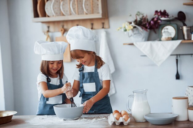 Enfants de la famille en uniforme de chef blanc préparant la nourriture dans la cuisine.