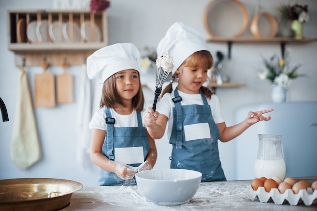 Enfants de la famille en uniforme de chef blanc préparant la nourriture dans la cuisine.