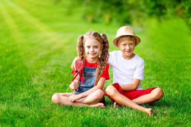 Enfants fille et garçon blond avec un grand coeur de sucette en été sur la pelouse sur l'herbe verte le concept de l'espace de vacances de la Saint-Valentin pour le texte
