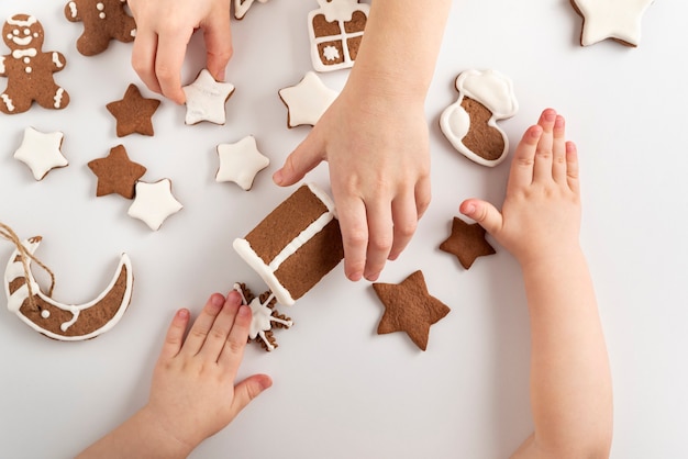 Les enfants font du pain d'épice. Les mains des enfants et les biscuits au pain d'épice glacés au sucre sur fond blanc, vue de dessus.