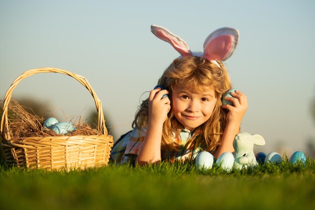 Enfants garçon chasser les oeufs de pâques dans le parc portant sur l'herbe sur fond de ciel avec copie espace enfant avec des oreilles de lapin