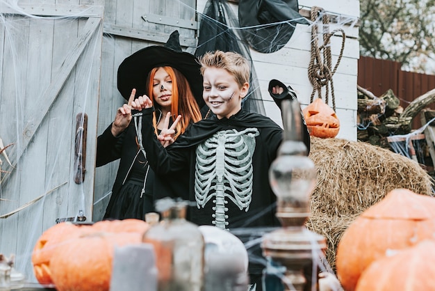 Enfants un garçon dans un costume de squelette et une fille dans un costume de sorcière s'amusant à une fête d'Halloween sur le porche décoré