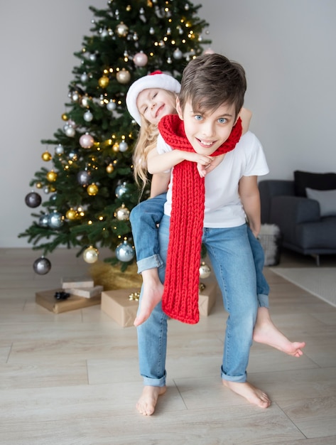 Enfants - un garçon et une fille jouent près de l'arbre de Noël. Intérieur du salon avec sapin de Noël et décorations. Nouvelle année. Donner en cadeau.