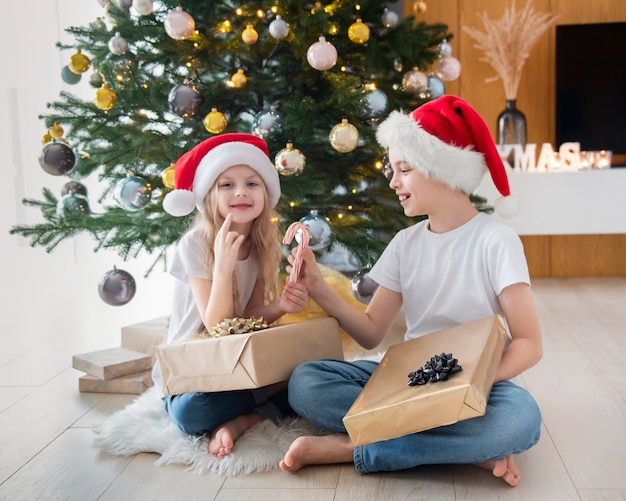 Enfants - un garçon et une fille jouent près de l'arbre de Noël. Intérieur du salon avec sapin de Noël et décorations. Nouvelle année. Donner en cadeau.