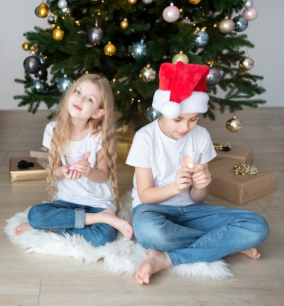 Enfants - un garçon et une fille jouent près de l'arbre de Noël. Intérieur du salon avec sapin de Noël et décorations. Nouvelle année. Donner en cadeau.