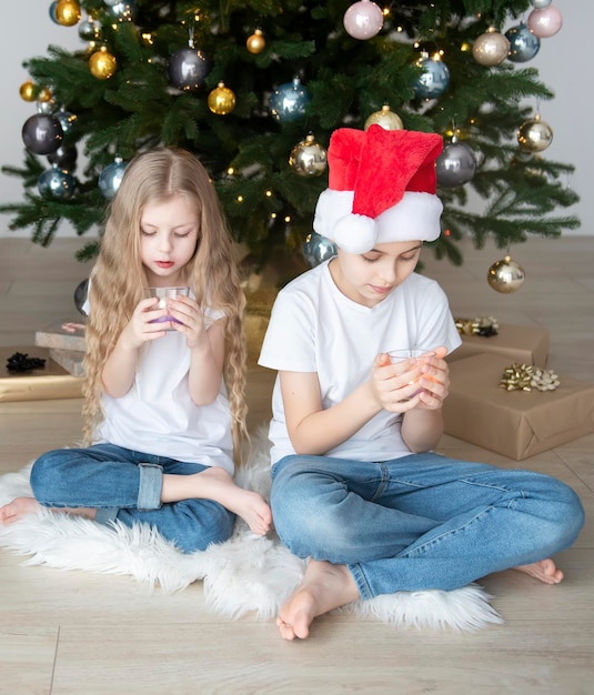 Enfants - un garçon et une fille jouent près du sapin de Noël. Intérieur du salon avec sapin de Noël et décorations. Nouvelle année. Donner en cadeau.