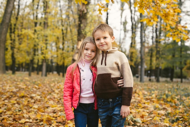 Les enfants un garçon et une fille s'amusent et s'embrassent dans la forêt d'automne parmi les feuilles tombées