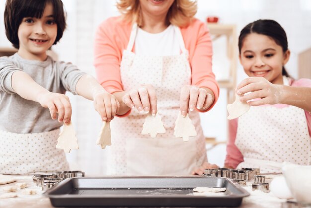 Enfants avec la grand-mère mettant des biscuits sur le plateau de cuisson