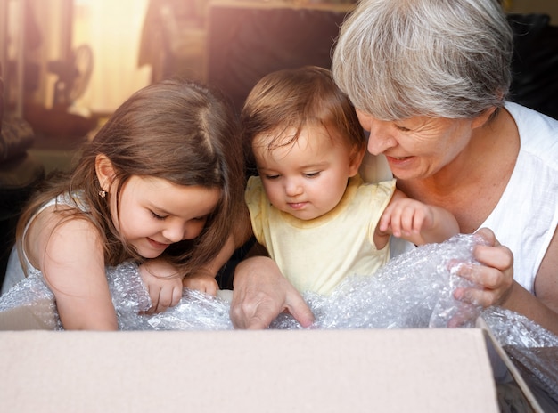 Les enfants et la grand-mère ouvrent la boîte. femme et petites-filles regardent dans le colis