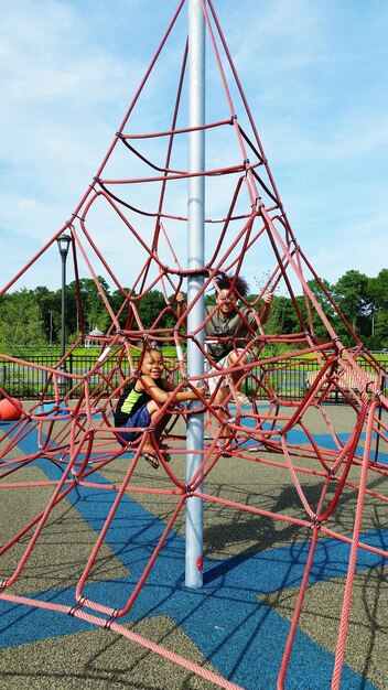 Photo des enfants grimpant sur le gymnase de la jungle contre le ciel dans le parc