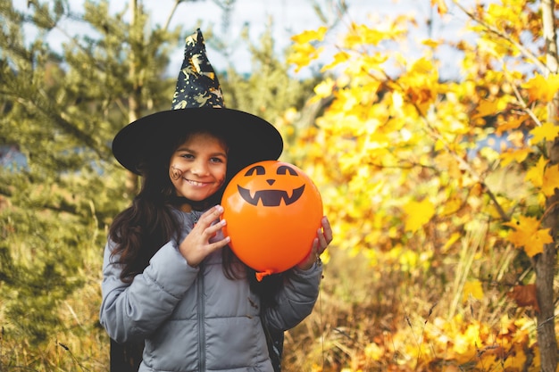 Enfants d'Halloween. Portrait fille souriante aux cheveux bruns en chapeau de sorcière avec ballon citrouille.
