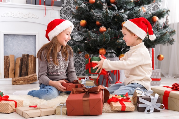 Des enfants heureux en chapeaux de père Noël déballant des cadeaux de Noël