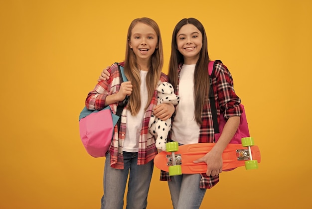 Des enfants heureux en chemise à carreaux décontractée portent un jouet de sac à dos et un style de vie décontracté de penny board