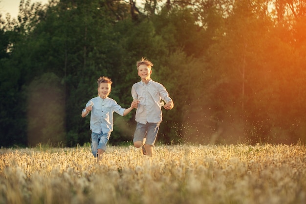 Enfants heureux courir autour du terrain avec dandalions onsummer sunset.