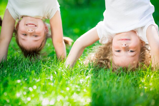 Enfants heureux debout à l'envers sur l'herbe verte Enfants souriants s'amusant dans le parc du printemps Concept de mode de vie sain