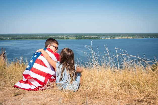 Des enfants heureux avec le drapeau américain sont assis dans un champ sur le fond de la baie