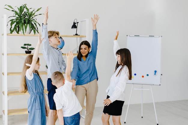 Enfants heureux et éducateur levant les mains debout dans une salle de classe moderne En-tête de site Web avec portrait de groupe d'enseignants et d'élèves joyeux ayant des activités amusantes