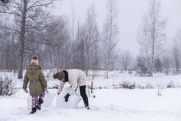 Des enfants heureux font un bonhomme de neige dans un champ enneigé à la campagne.