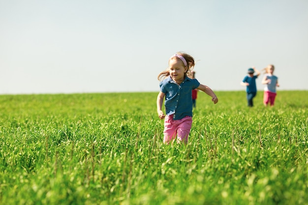 Des enfants heureux de garçons et de filles courent dans le parc sur l'herbe par une journée d'été ensoleillée