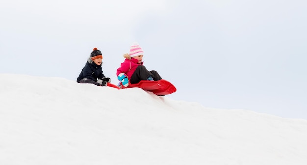 Des enfants heureux glissant sur des traîneaux en bas de la colline en hiver.