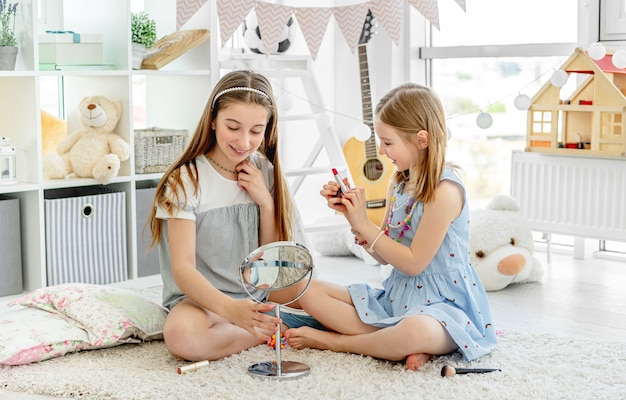 Enfants heureux jouant avec le rouge à lèvres de maquillage dans la chambre confortable