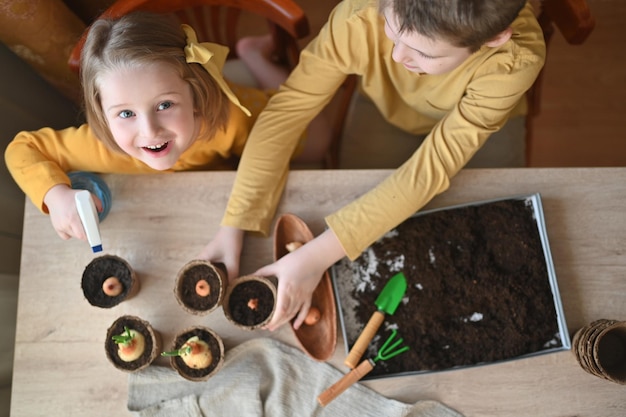 Photo des enfants heureux plantent des plantes à la maison, une fille et un garçon sèment des graines dans des pots de jardinage naturels devoirs amusants avec la famille et l'école de biologie