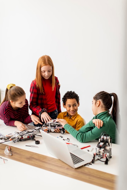 Des enfants heureux programmant des jouets électriques et des robots en classe de robotique