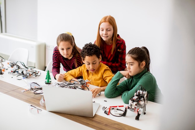 Des enfants heureux programmant des jouets électriques et des robots en classe de robotique