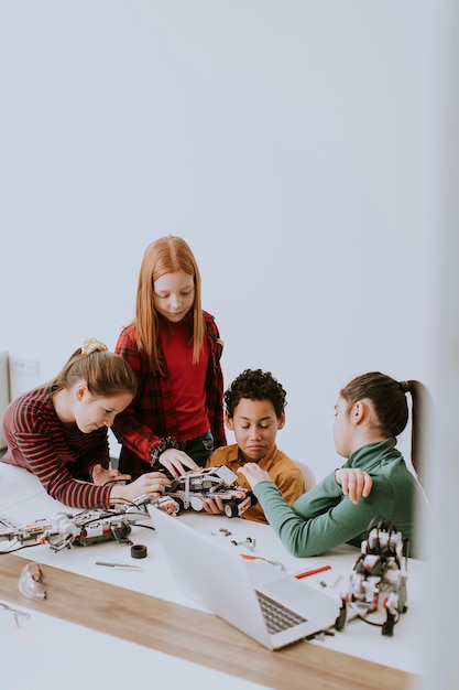 Des enfants heureux programmant des jouets électriques et des robots en classe de robotique