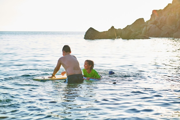 Enfants heureux regardant la caméra jouant dans la mer avec bodyboard. Les enfants s'amusent à l'extérieur. Concept de vacances d'été et mode de vie sain.
